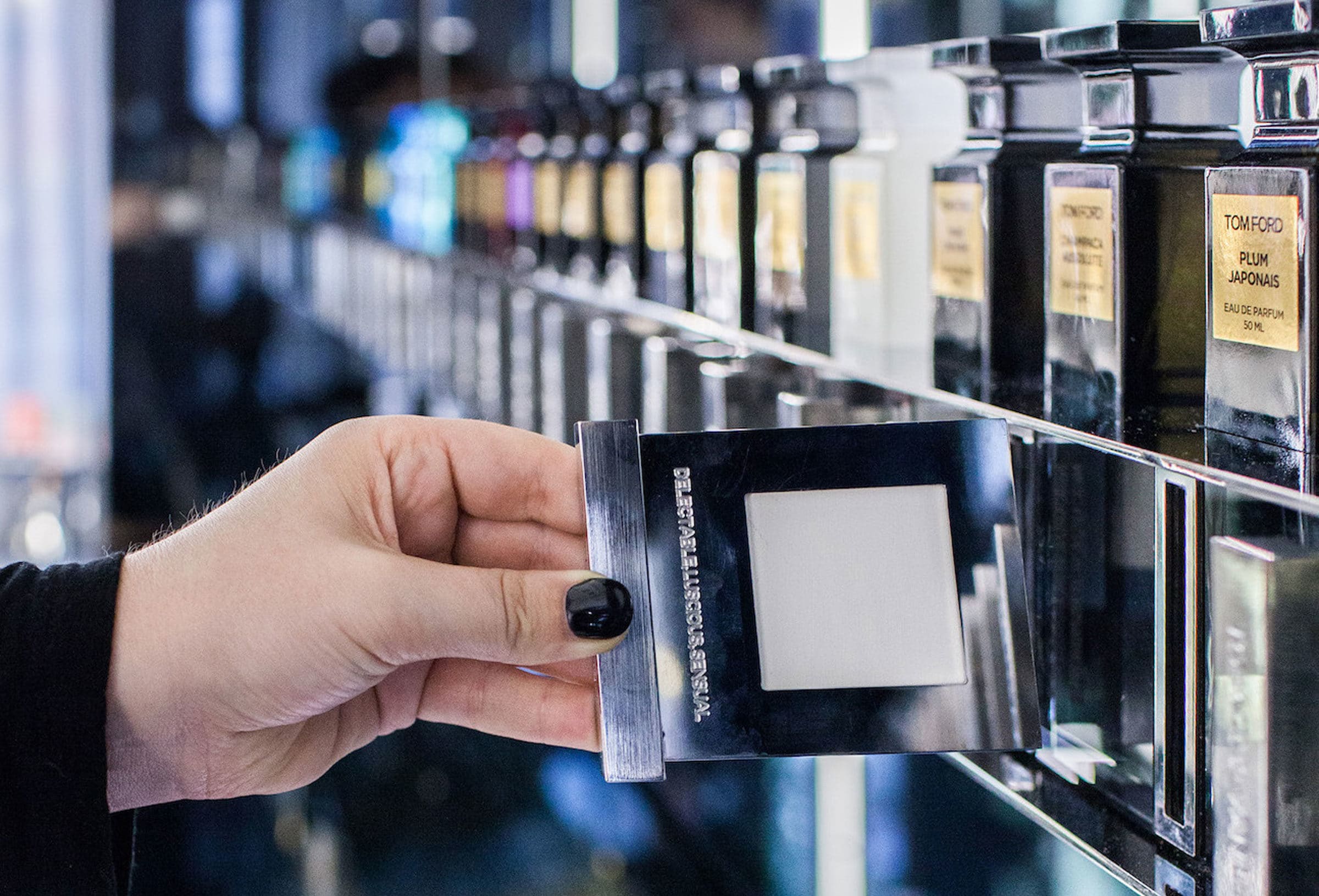 Hand holding a scent strip in front of the fragrance shelf